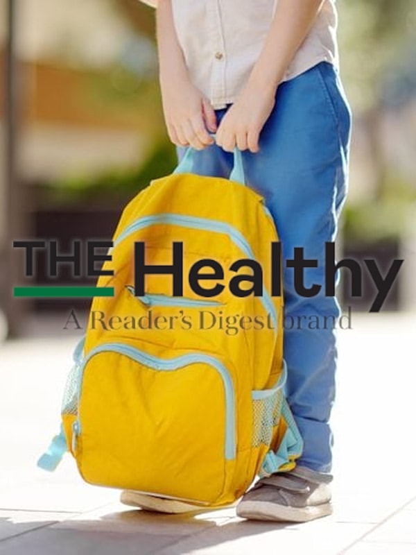 Child holding a bright yellow backpack outdoors.