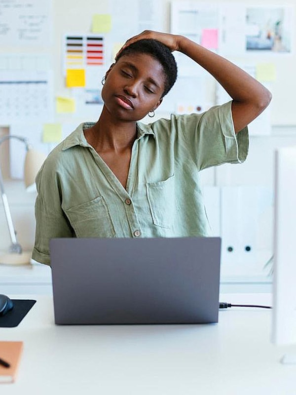 Woman stretching while working on laptop.