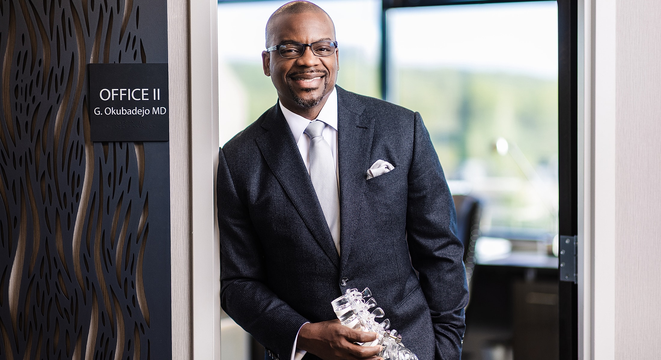 Doctor standing in office doorway, smiling confidently.