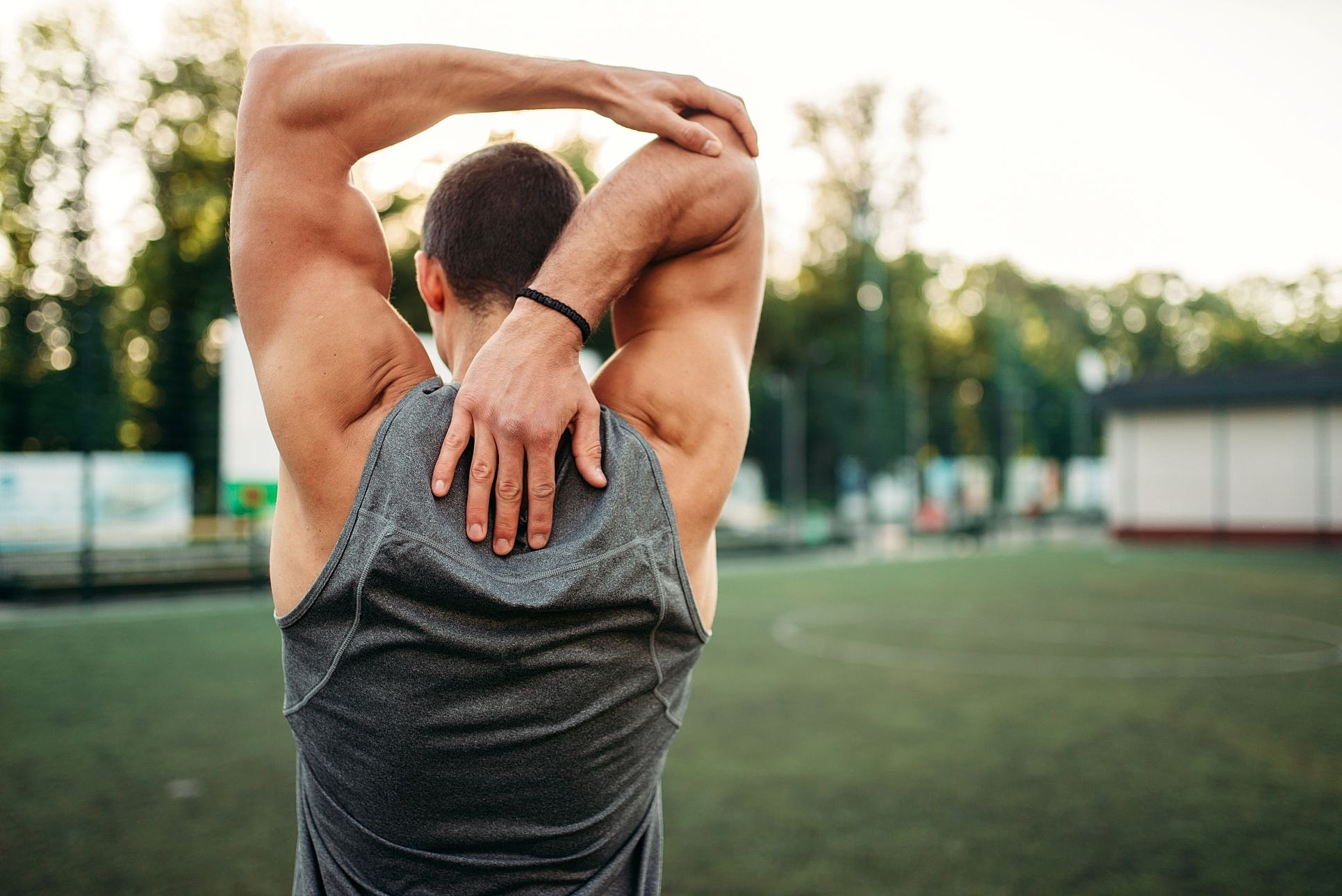 A man in a gray tank top performs overhead stretches outdoors, after physical therapy and conservative recovery for a herniated disc.